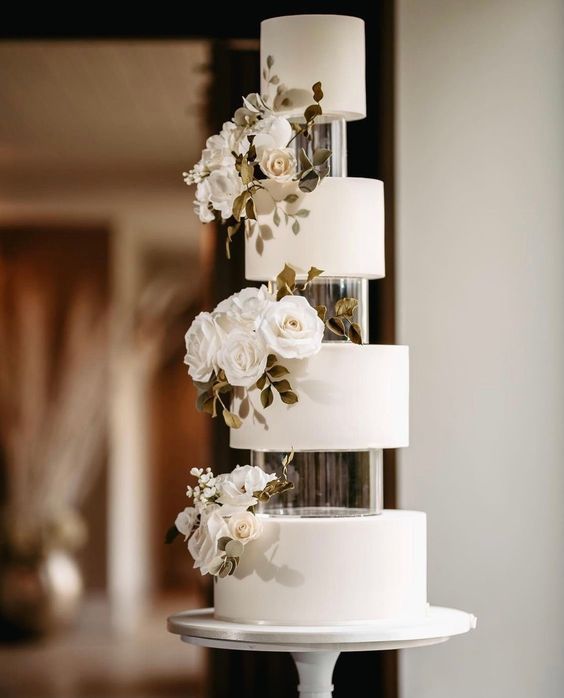 a beautiful and elegant white wedding cake with tiers seaparated with clear acrylic stands, with white blooms and greenery