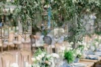 a beautiful botanical wedding venue with hanging greenery and white blooms, candle lanterns, white floral centerpieces and blue linens