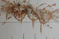 a beautiful dried grass and bloom wedding installation with dried grasses, lunaria, pampas grass, branches and some seed pods, also dried