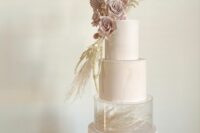 a blush wedding cake with a pattern, a clear acrylic separator with some dried grasses, dusty pink fronds and blooms plus grass on top