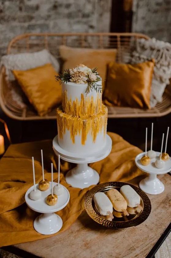 a boho wedding cake with yellow and rust textural patterns and neutral blooms and greenery on top