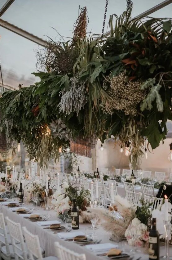 a boho wedding venue with a greenery and grass installation, greenery and pampas grass decor and candles