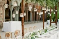 a botanical wedding venue with hanging candles, greenery, a greenery and white bloom runner and white linens is fresh and chic