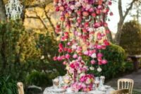 a bright and lush floral chandelier of bold red, pink, purple and blush blooms that touches the table and acts as a centerpiece, too