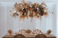 a catchy and cool dried flower wedding installation with peachy and blush blooms, greenery, dark flowers and pampas grass