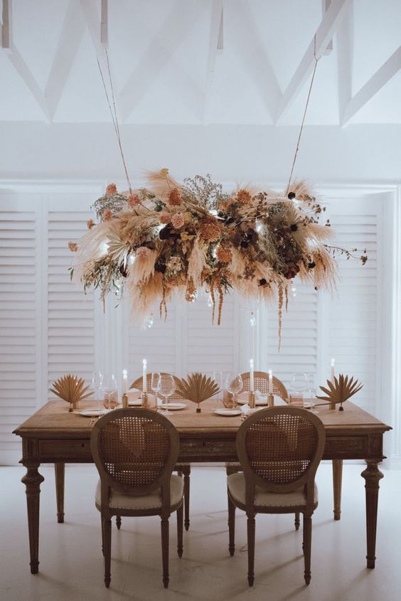 a catchy and cool dried flower wedding installation with peachy and blush blooms, greenery, dark flowers and pampas grass