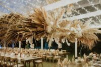 a catchy overhead wedding installation with pampas grass, dried fronds and white orchids is a very bold and cool idea for a boho wedding