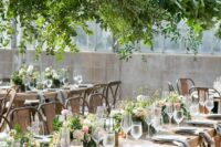 a catchy wedding reception with an overhead greenery installation, greenery and pink blooms on the table and grey napkins