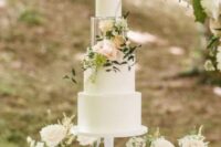 a classy white wedding cake with a clear acrylic separator filled with neutral and blush blooms and greenery for a modern wedding
