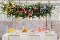 a colorful floral installation with greenery, yellow, orange, pink, burgundy, lilac and blue florals, branches and greenery for a colorful wedding
