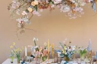 a cool and bright spring wedding tablescape with bright and pastel blooms, white and yellow candles, lavender glasses and an overhead floral installation that matches