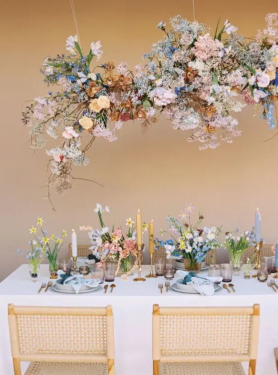 a cool and bright spring wedding tablescape with bright and pastel blooms, white and yellow candles, lavender glasses and an overhead floral installation that matches