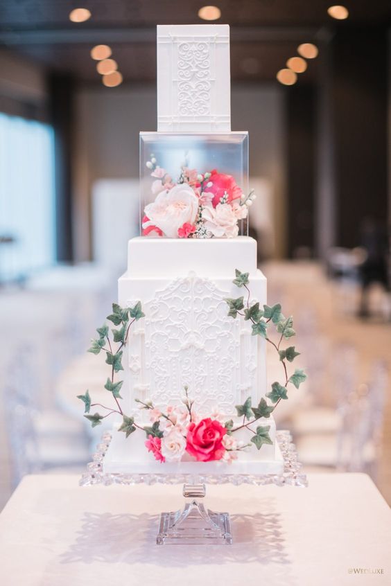a creative secret garden wedding cake with patterned tiers, a clear acrylic stand with blush and coral blooms and leaves