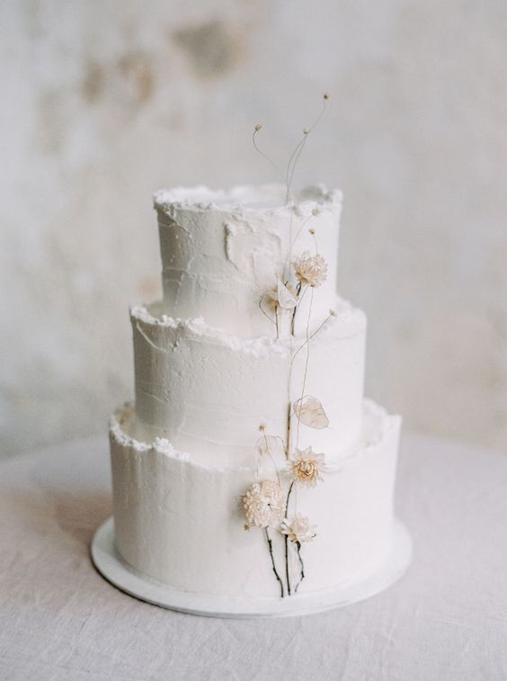 a delicate white textural wedding cake with a raw edge and some neutral dried blooms attached is a lovely idea for a spring or summer