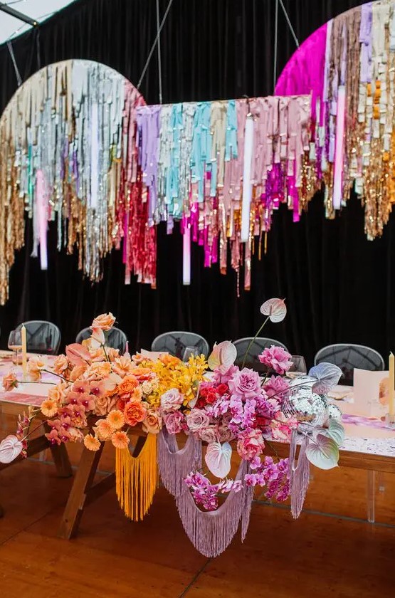 a fantastic and bright wedding reception space with colorful tinsel streamers and matching colorful blooms on the table