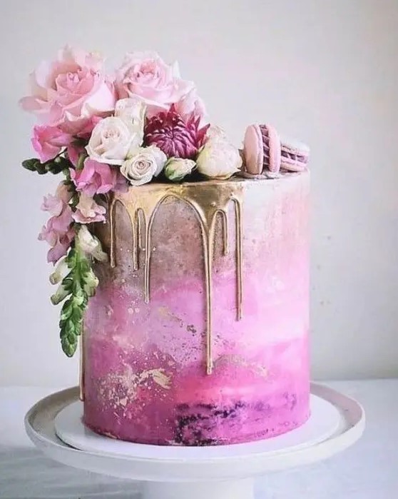 a fantastic hot pink wedding cake with an ombre effect, gold drip, pink macarons and pink blooms on top for a glam wedding