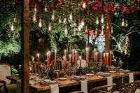 a gorgeous wedding reception with greenery and bold blooms over the table, bulbs, red candles and greenery runners