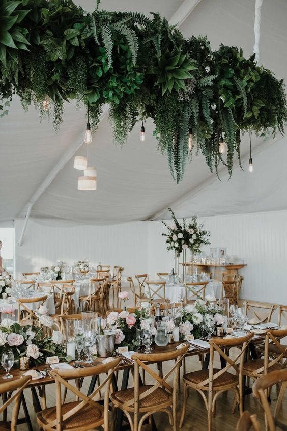 a lovely wedding tablescape with pink and white blooms and greenery, a super lush greenery wedding installation with bulbs hanging down