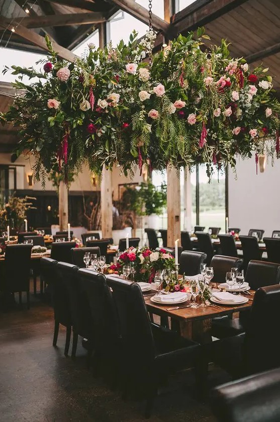 a lush greenery and floral overhead wedding decoration creates a strong wow effect, and an arrangement on the table echoes with it