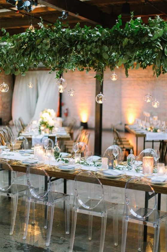 a lush greenery installation with hanging bubbles and candles is a very refreshing idea for an indoor wedding