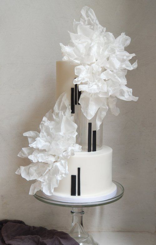 a luxurious black and white wedding cake with black stripes, a clear tier decorated with them, too, white sugar blooms on top