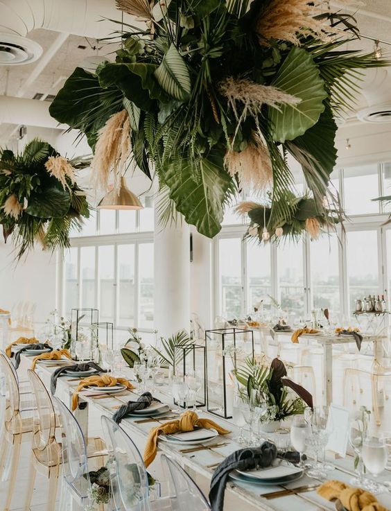 a modern wedding table setting with candle lanterns and mustard and grey napkins, fronds and pampas grass over the table
