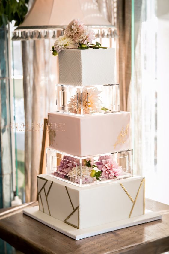 a modern white square wedding cake decorated in various ways, with clear lucite stands filled with fresh pink blooms