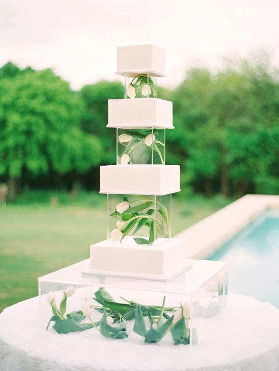 a modern white square wedding cake with clear acrylic stands and white tulips in them looks airy, refined and chic
