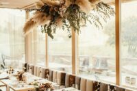 a pampas grass and greeneyr overhead wedding installation is a lovely decor idea for any wedding reception