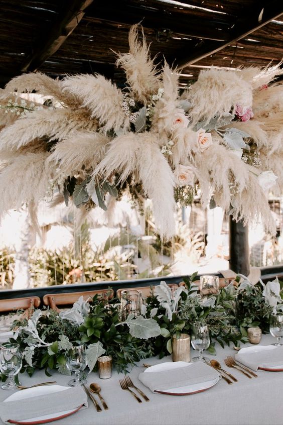 a pampas grass, greenery and blush rose overhead installation will pump your wedding reception and make it look more boho