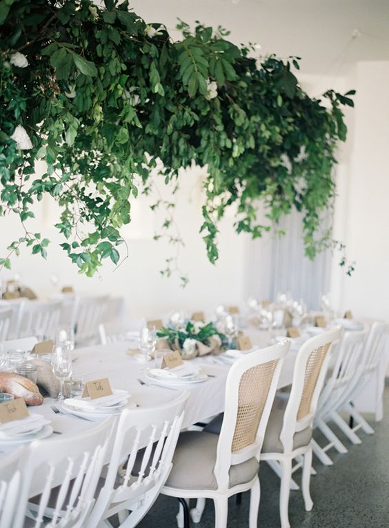 a refined neutral wedding tablescape with greenery on the table and a lush overhead installation over the table, too
