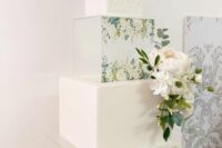 a refined white square wedding cake with clear acrylic stands with painted blooms, fresh white blooms and greenery is a chic and beautiful idea