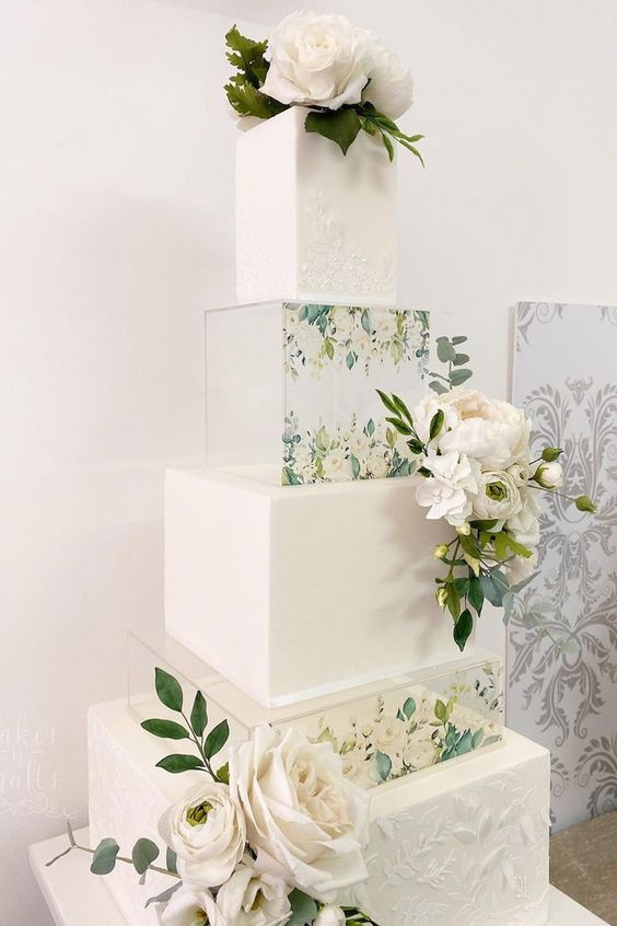 a refined white square wedding cake with clear acrylic stands with painted blooms, fresh white blooms and greenery is a chic and beautiful idea