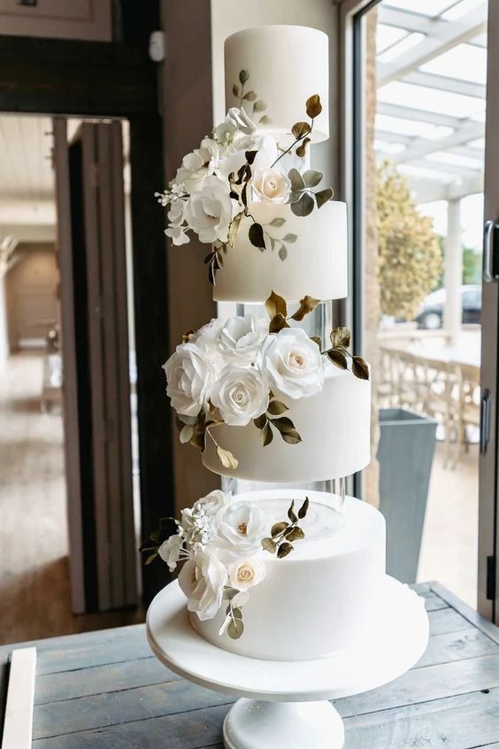 a round white wedding cake accented with clear acrylic separators, white roses and greenery is a very elegant and chic idea
