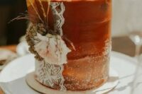 a rust textural wedding cake with sugar powder, lace, fresh and dried bloomsand grass for a fall boho wedding