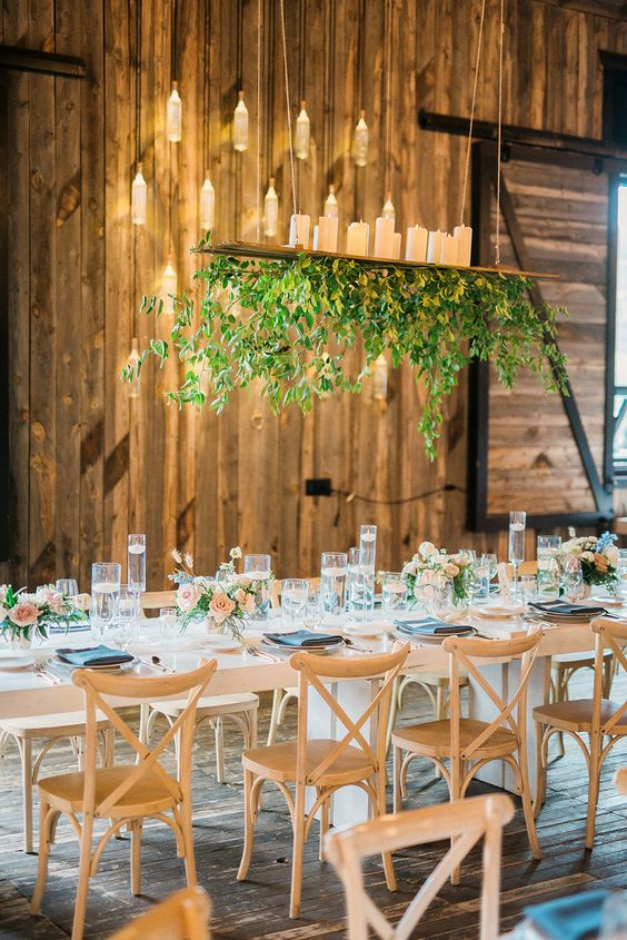 a rustic wedding tablescape with peachy roses, floating candles, a greenery overhead wedding insallation with pillar candles on top