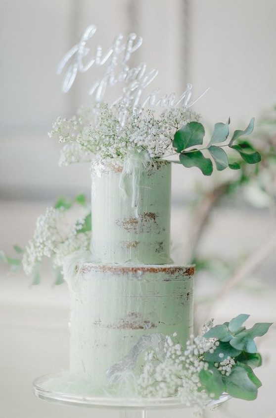 a semi-naked green wedding cake topped with white baby's breath, eucalyptus and an acrylic topper for a modern boho wedding