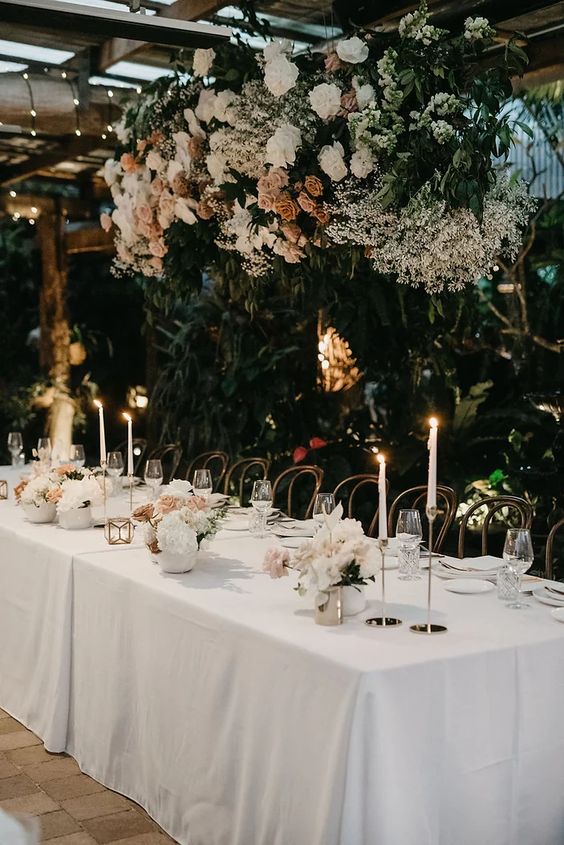 a sophisticated floral wedding installation with white and pink roses, baby's breath, greenery and matching arrangements on the table