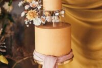 a sophisticated rust-colored wedding cake with a clear acrylic tier decorated with dried and fresh blooms and leaves, with a pink ribbon