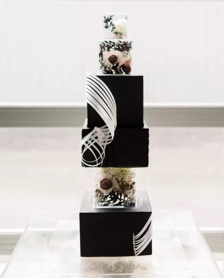 a square black wedding cake with white sugar swirls, clear acrylic separators with fresh blooms and greenery is a very modern solution