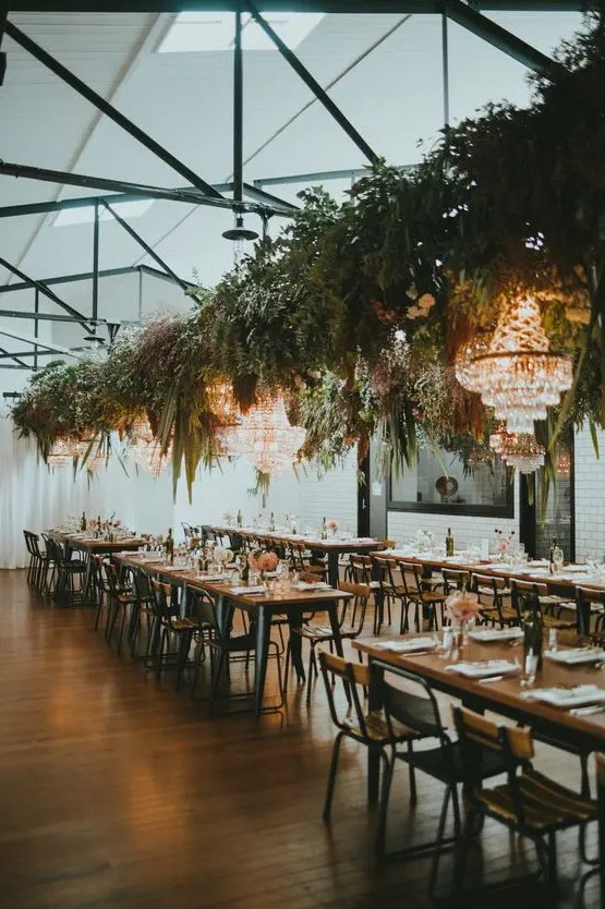 a stylish industrial venue with skylights, exposed metals, refined chandeliers, greenery installations