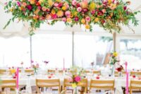 a super colorful and cool overhead floral installation with yellow, pink and purple blooms and greenery, branches and leaves is wow