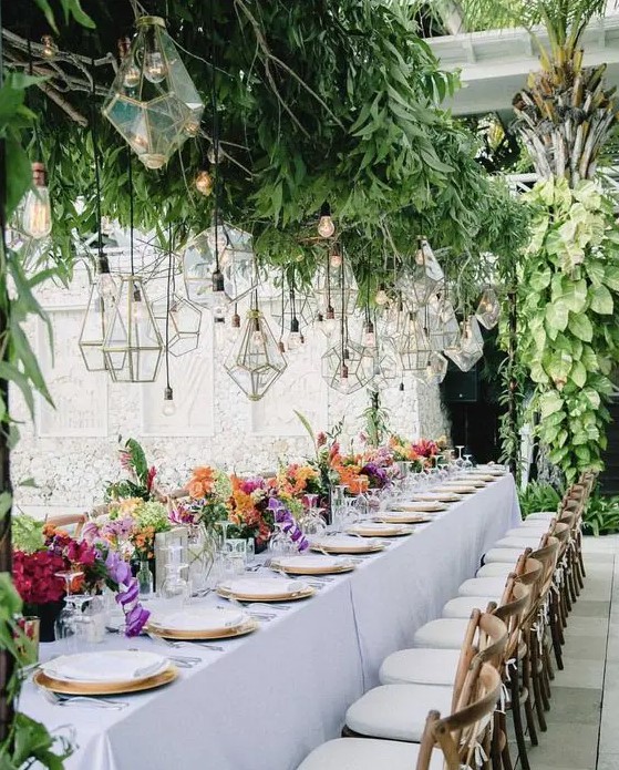 a super lush overhead greenery decoration with lots of bulbs and geometric lanterns hanging