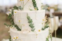 a white buttercream wedding cake decorated with greenery and wildflowers is a cool idea for a spring or summer wedding