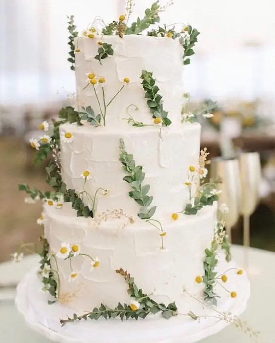 a white buttercream wedding cake decorated with greenery and wildflowers is a cool idea for a spring or summer wedding