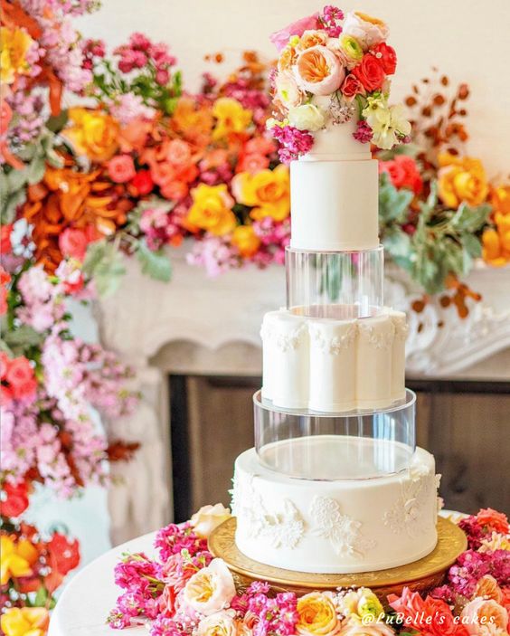 a white round wedding cake with clear tiers and with super bright flowers on top is a fantastic idea for a colorful wedding