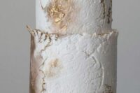 a white textural buttercream and gold wedding cake with a raw edge and some white blooms on top is a refined idea for a neutral wedding