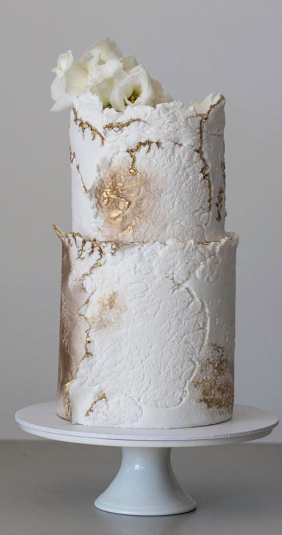 a white textural buttercream and gold wedding cake with a raw edge and some white blooms on top is a refined idea for a neutral wedding