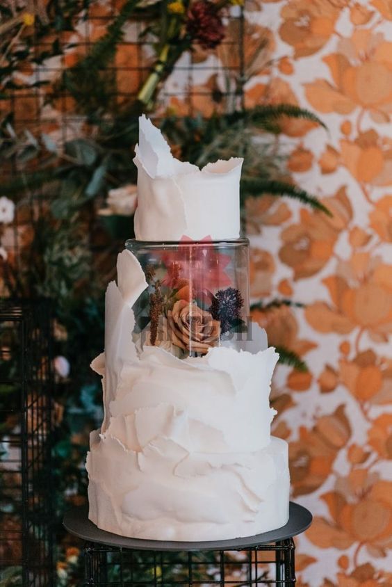 a white textural wedding cake with edges and a clear acrylic separator with rust and dark blooms is a fantastic idea for a refined wedding
