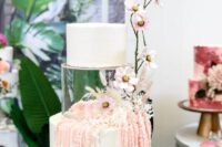 a white wedding cake with a clear acrylic tier decorated with pink blooms and blooming branches on the outside